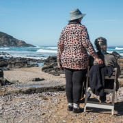 Senior woman with dementia sitting on a chair and her caregiver by the sea