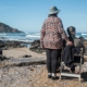 Senior woman with dementia sitting on a chair and her caregiver by the sea